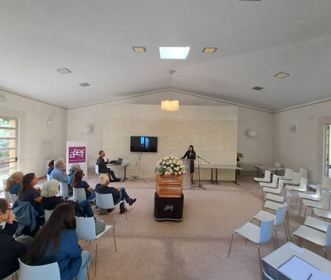 erimonia funebre nella sala del commiato A.Se.F., con feretro adornato di fiori e partecipanti seduti.