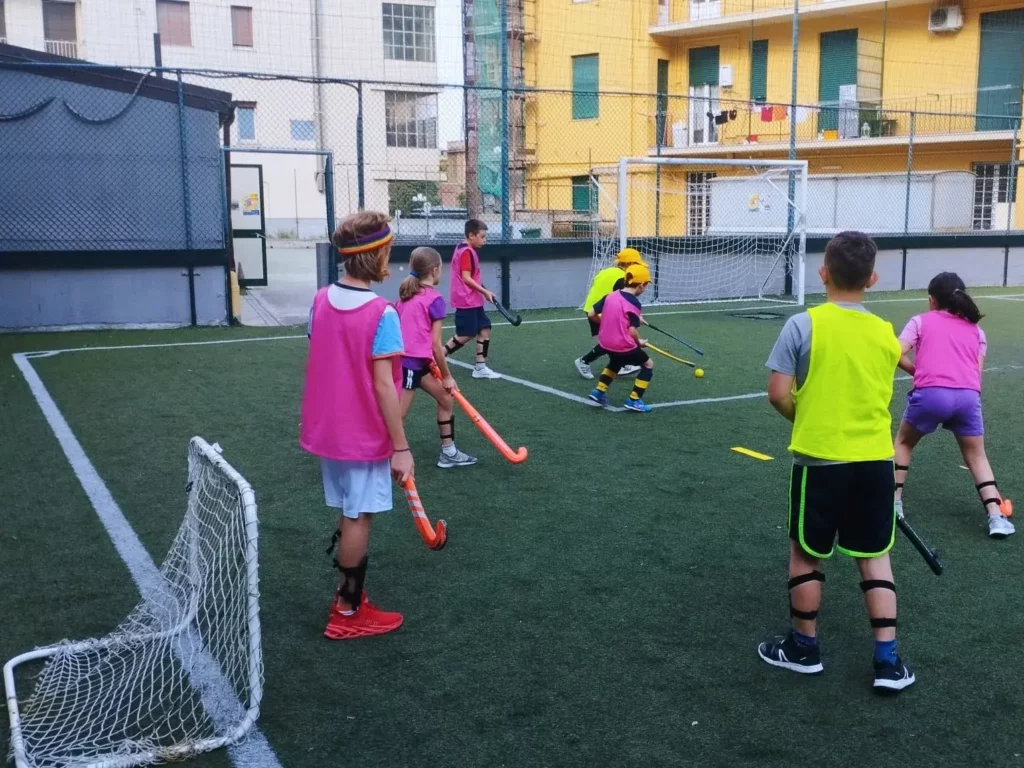 Bambini impegnati in un’attività di avviamento all’hockey su un campo in erba sintetica.