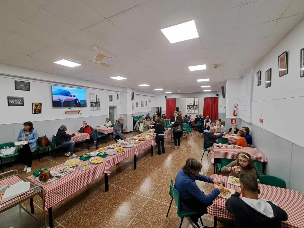 Sala della Cucina Popolare Genovese con tavoli apparecchiati e partecipanti alla serata di inaugurazione.