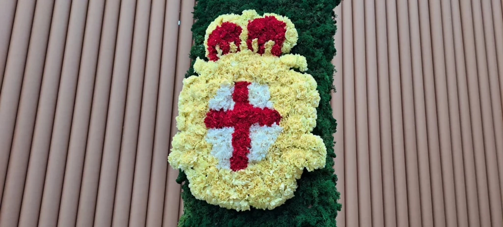 Stemma di Genova composto da fiori bianchi, rossi e gialli sulla Lanterna verde.
