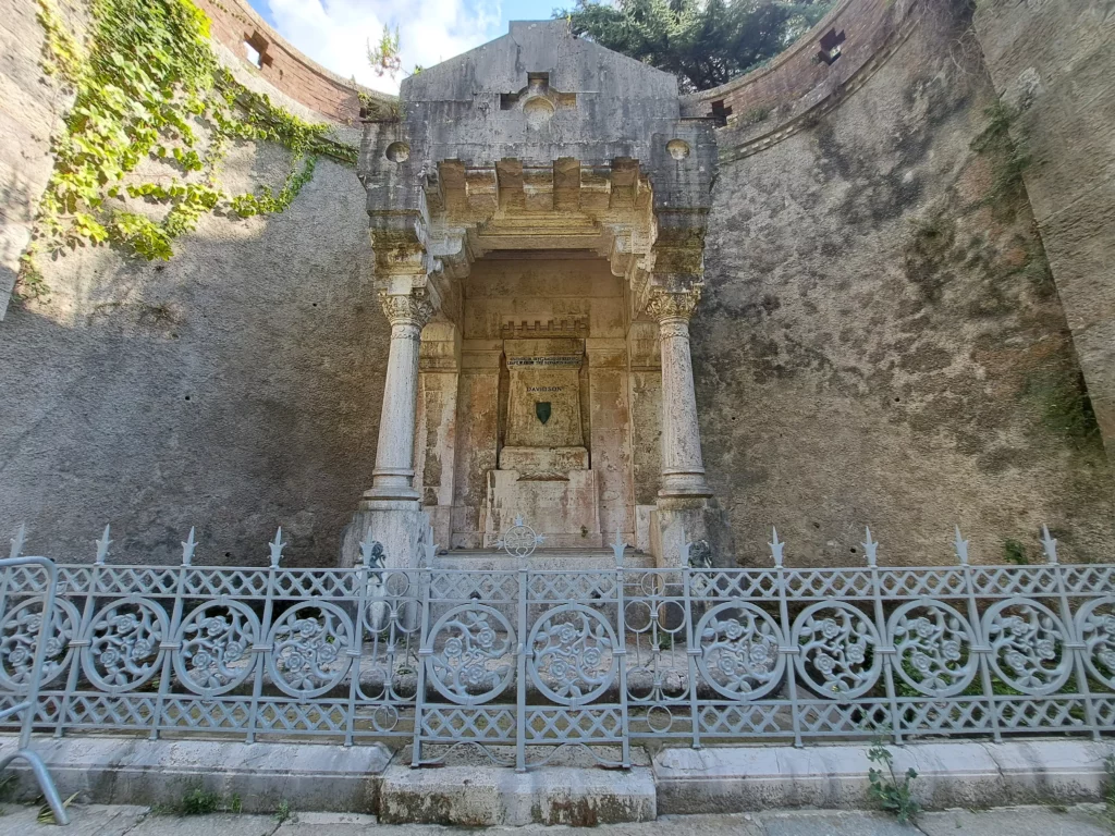 Monumento funerario in pietra dietro una cancellata decorata nel cimitero di Staglieno.