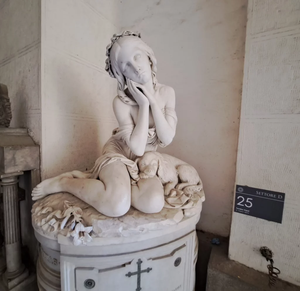 Scultura in marmo di una giovane seduta con il volto appoggiato alle mani, a Staglieno.