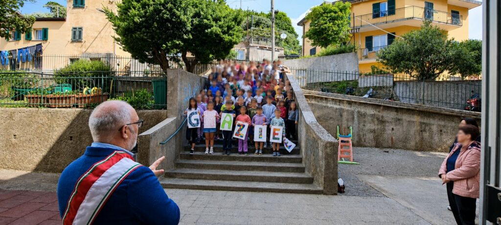 Bambini della scuola di Crevari sulle scale con cartelli che compongono la parola “Grazie”.
