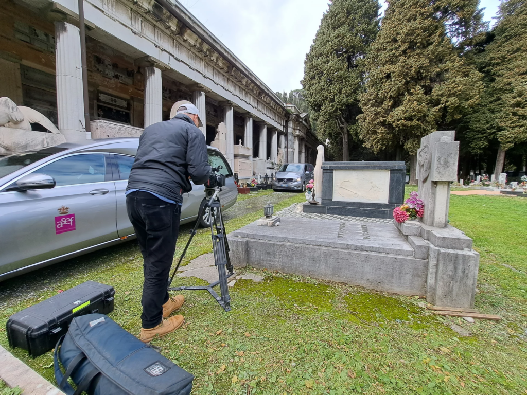 Operatore con telecamera accanto a un’autofunebre A.Se.F. sul set a Staglieno.