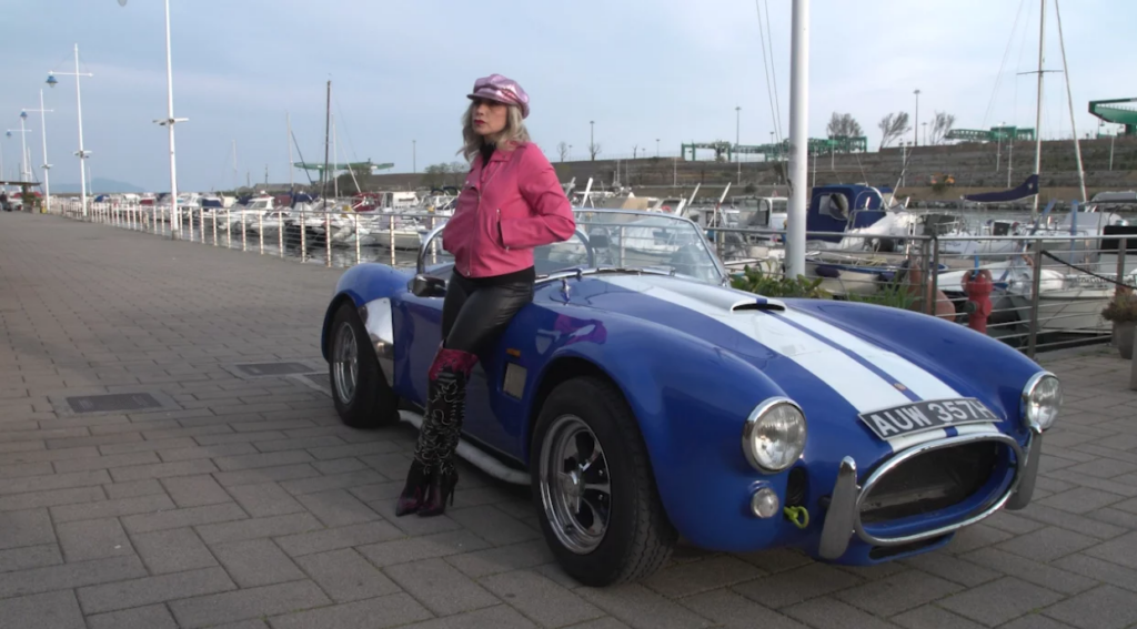 Protagonista di “Lady Cobra” accanto a una Shelby Cobra blu con strisce bianche.