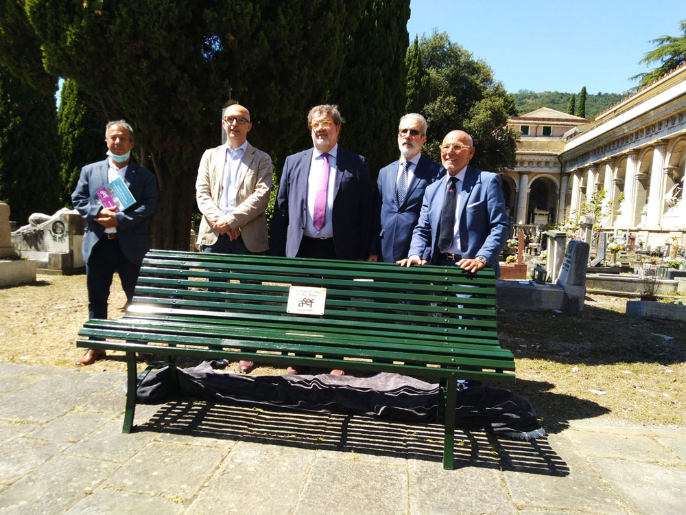 Partecipanti alla cerimonia dietro una panchina commemorativa per le vittime del ponte Morandi.
