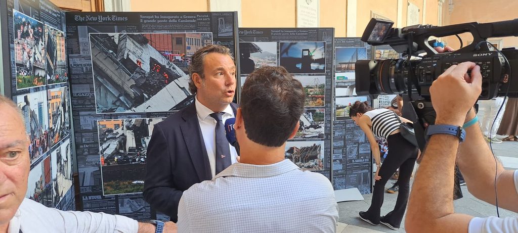 Un ospite viene intervistato davanti ai pannelli della mostra fotografica sul Ponte Morandi.
