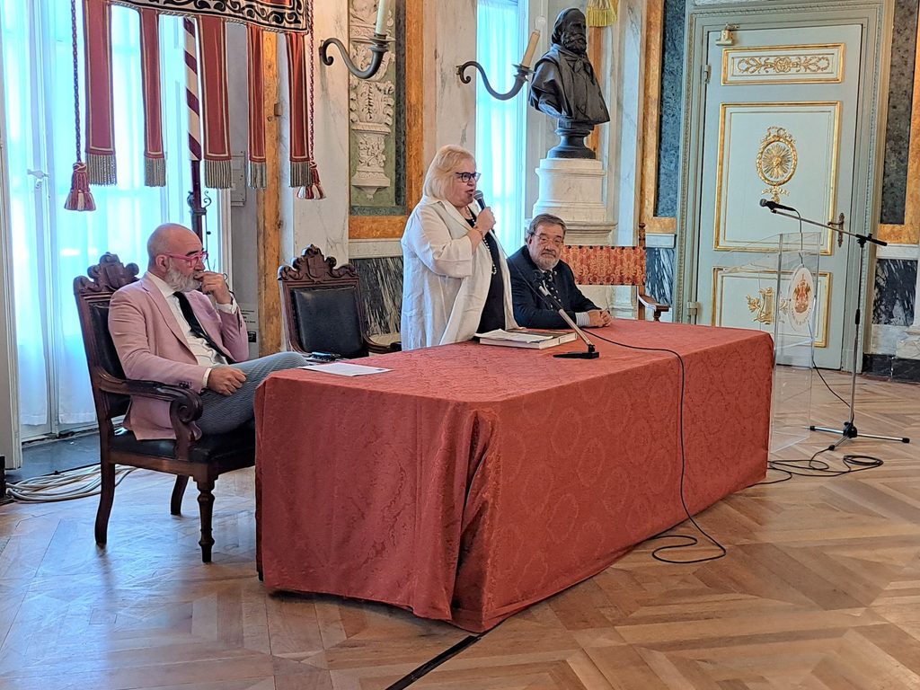 Una relatrice parla al microfono al tavolo della conferenza su Erbari Svelati.