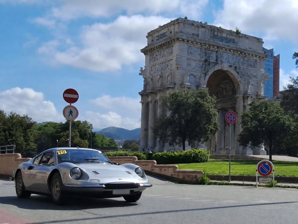 Auto sportiva d’epoca grigia percorre la strada accanto all’Arco della Vittoria di Genova.