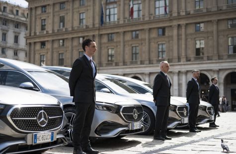 Operatori funebri in abito scuro accanto a una fila di autofunebri.